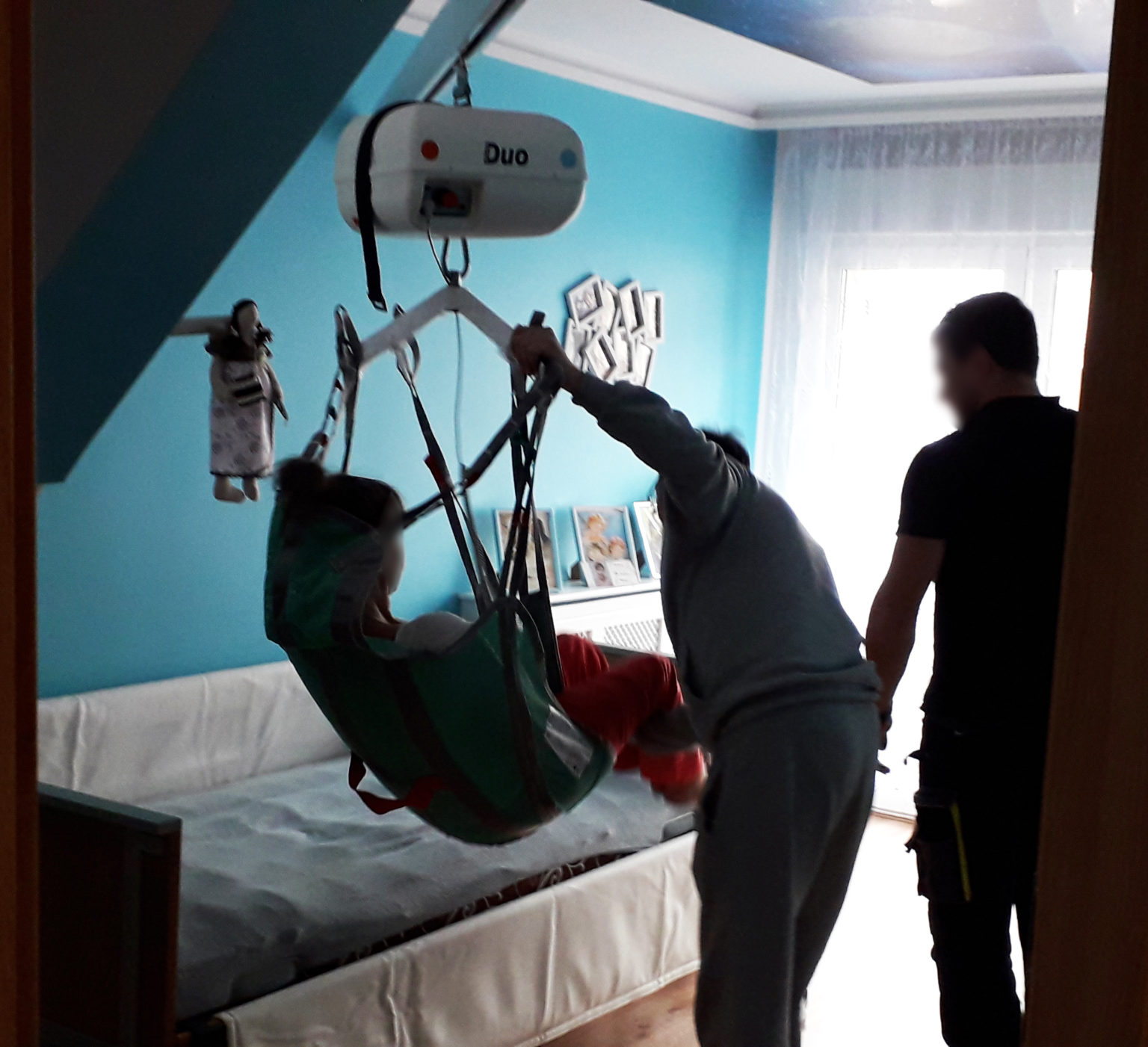 Osoba korzystająca z podnośnika w pokoju, pomoc przy transferze.