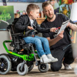 Chłopiec na wózku inwalidzkim rysuje z dorosłym w artystycznym otoczeniu.