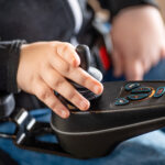 Ręka na joysticku w wózku inwalidzkim, kontrolująca ruch.