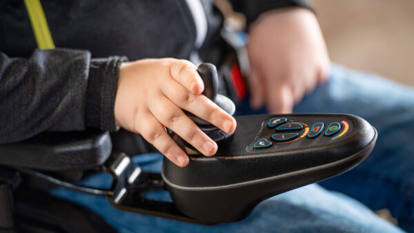 Ręka na joysticku w wózku inwalidzkim, kontrolująca ruch.