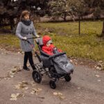 Mama prowadzi wózek dziecięcy po drodze w parku. Jesienna sceneria.