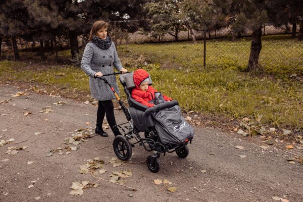 Mama prowadzi wózek dziecięcy po drodze w parku. Jesienna sceneria.