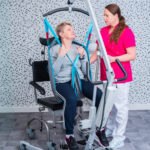 Kobieta w urządzeniu rehabilitacyjnym z pomocą terapeutki.