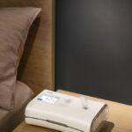 Urządzenie do terapii CPAP na stoliku nocnym obok łóżka.