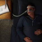 Mężczyzna śpiący w piżamie z maską CPAP obok łóżka.