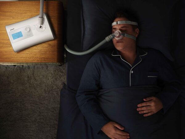 Mężczyzna śpiący w piżamie z maską CPAP obok łóżka.