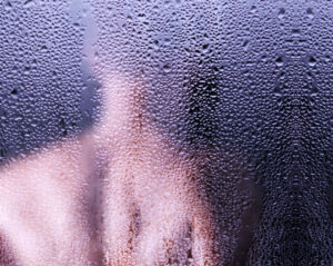 Zamglona szyba z wyraźnymi kroplami wody, przysłaniająca kontury.