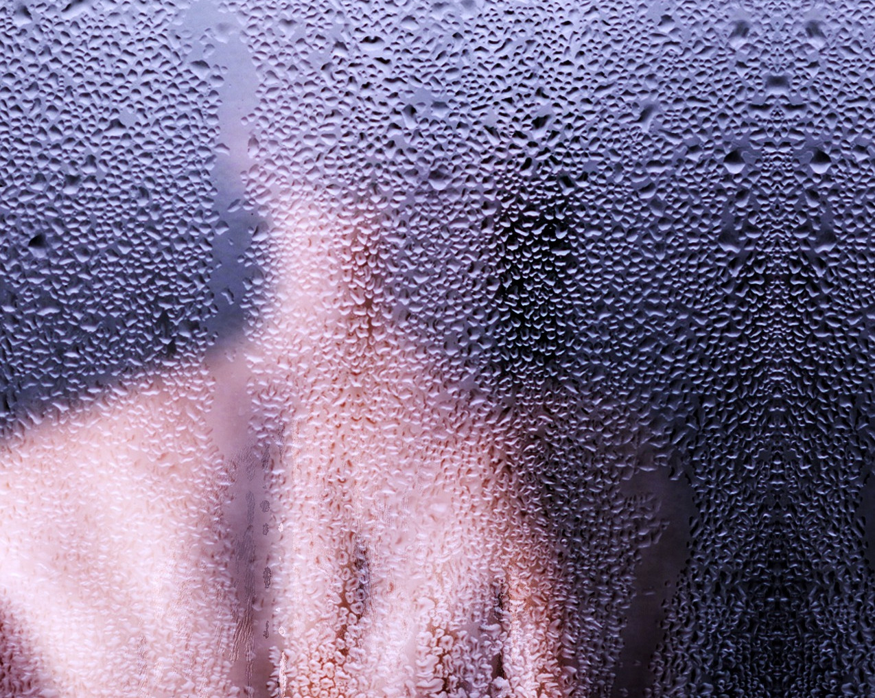 Zamglona szyba z wyraźnymi kroplami wody, przysłaniająca kontury.